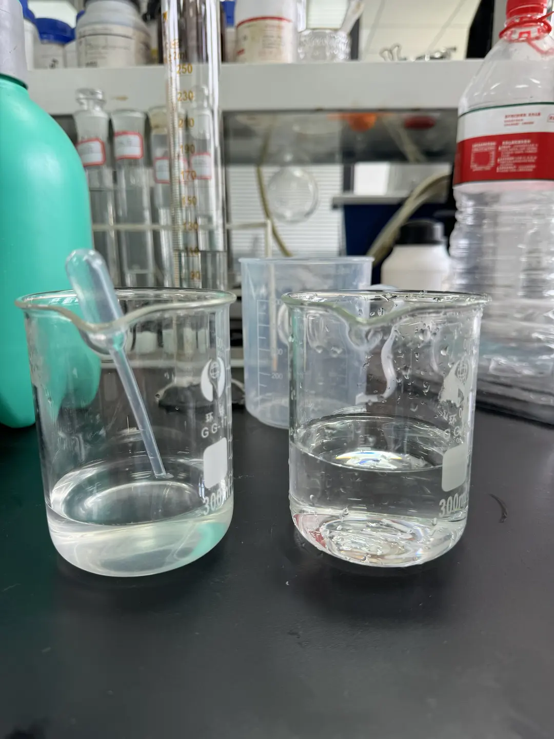 Two clear glasses of liquid on a dark lab bench