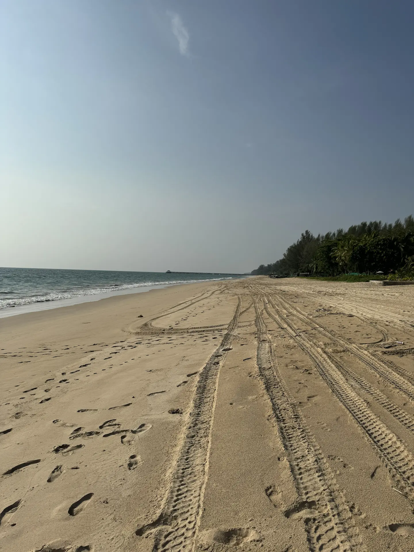 Empty Hội An beach with footprints, pale sand, teal water, green tree line