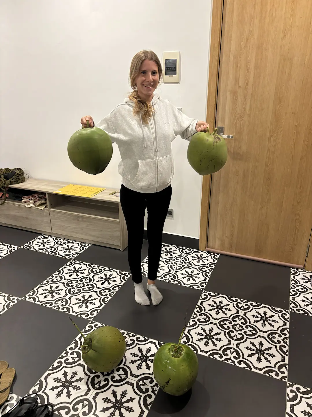 Jenny holding freshly harvested coconuts in a tiled room