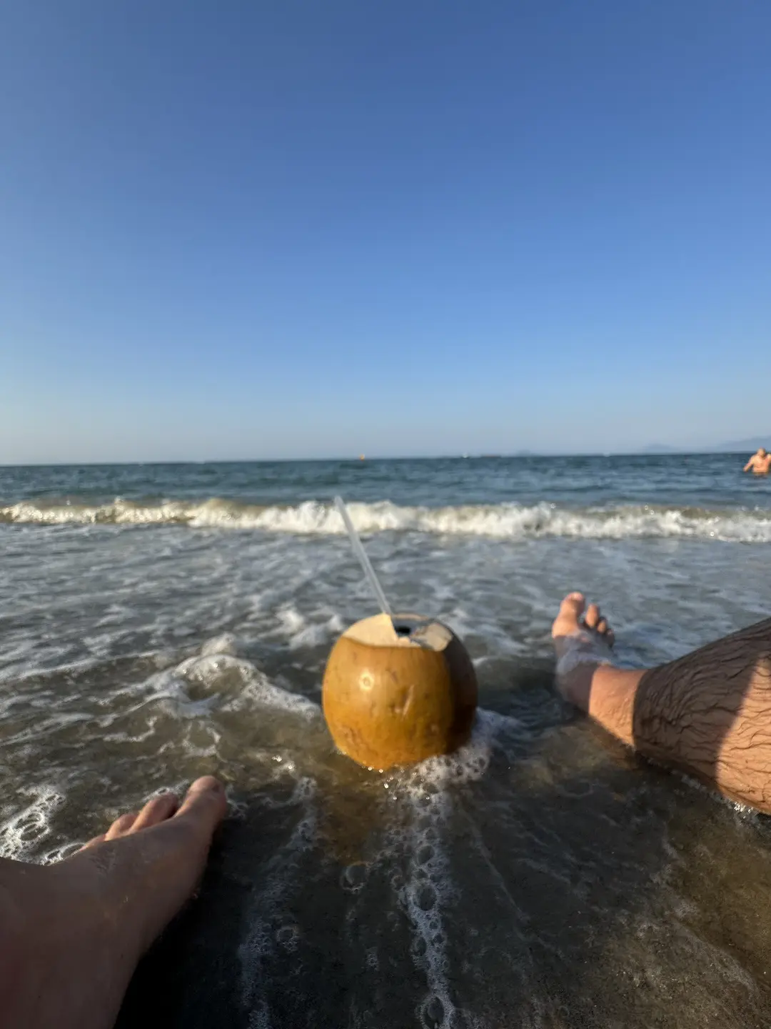 Coconut on white plate at beach bar, thatched umbrellas, blue sky