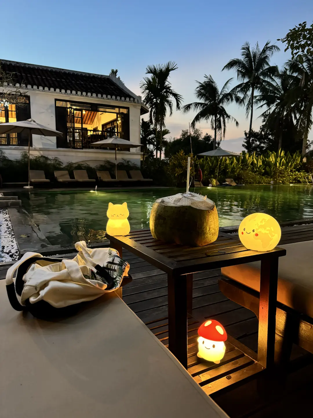 Coconuts on a table at dusk, resort pool and villa behind, warm lantern light